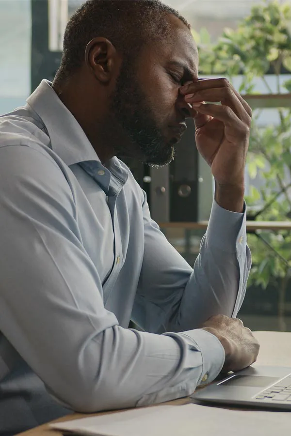 Chronic-Fatigue-Treatment A black man rubbing the top of his nose at his desk, experiencing chronic fatigue in Newfoundland.