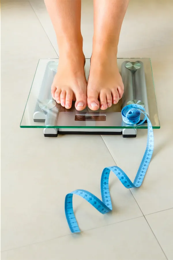 Weight-Loss-Resistance-Treatment Close-up of a woman's feet in Newfoundland standing on a scale, with measuring tape by her toes, getting treatment for weight loss resistance.